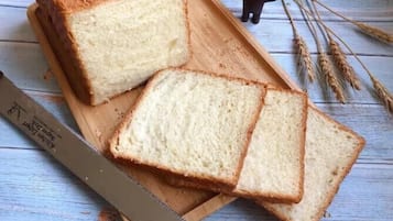 Una pagnotta di pane bianco su un tagliere di legno, con una lama di sega, spighe di grano e una statuina di un orso.
