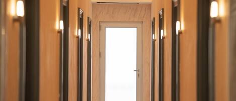 A hotel hallway with a central door, flanked by mirrored panels and wall-mounted lights.