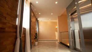 A modern hallway with a brick wall, a potted plant, and a stainless steel elevator. - KAME HOTEL BELGRADE (Belgrade)