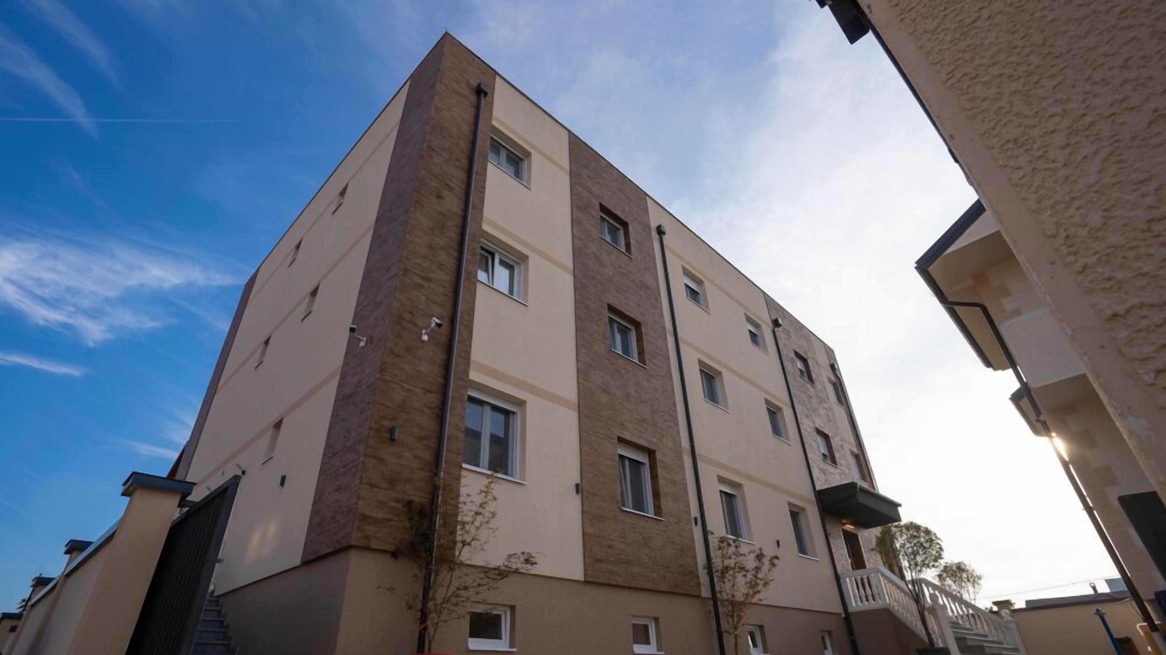Ein mehrstöckiges Gebäude mit modernem architektonischen Design, das eine Kombination aus beige- und braunen Fassaden, zahlreichen Fenstern und Balkonen aufweist.
