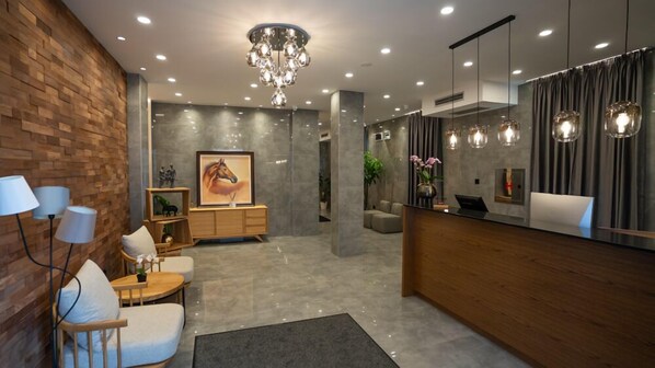 A modern reception area with a wooden reception desk, a chandelier, and a seating area with a white sofa and a small table.