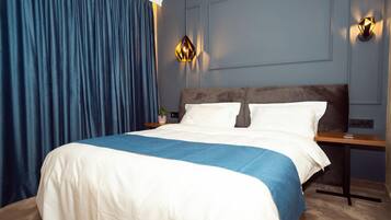 A modern hotel room with a large bed, blue curtains, and two wall-mounted lights.