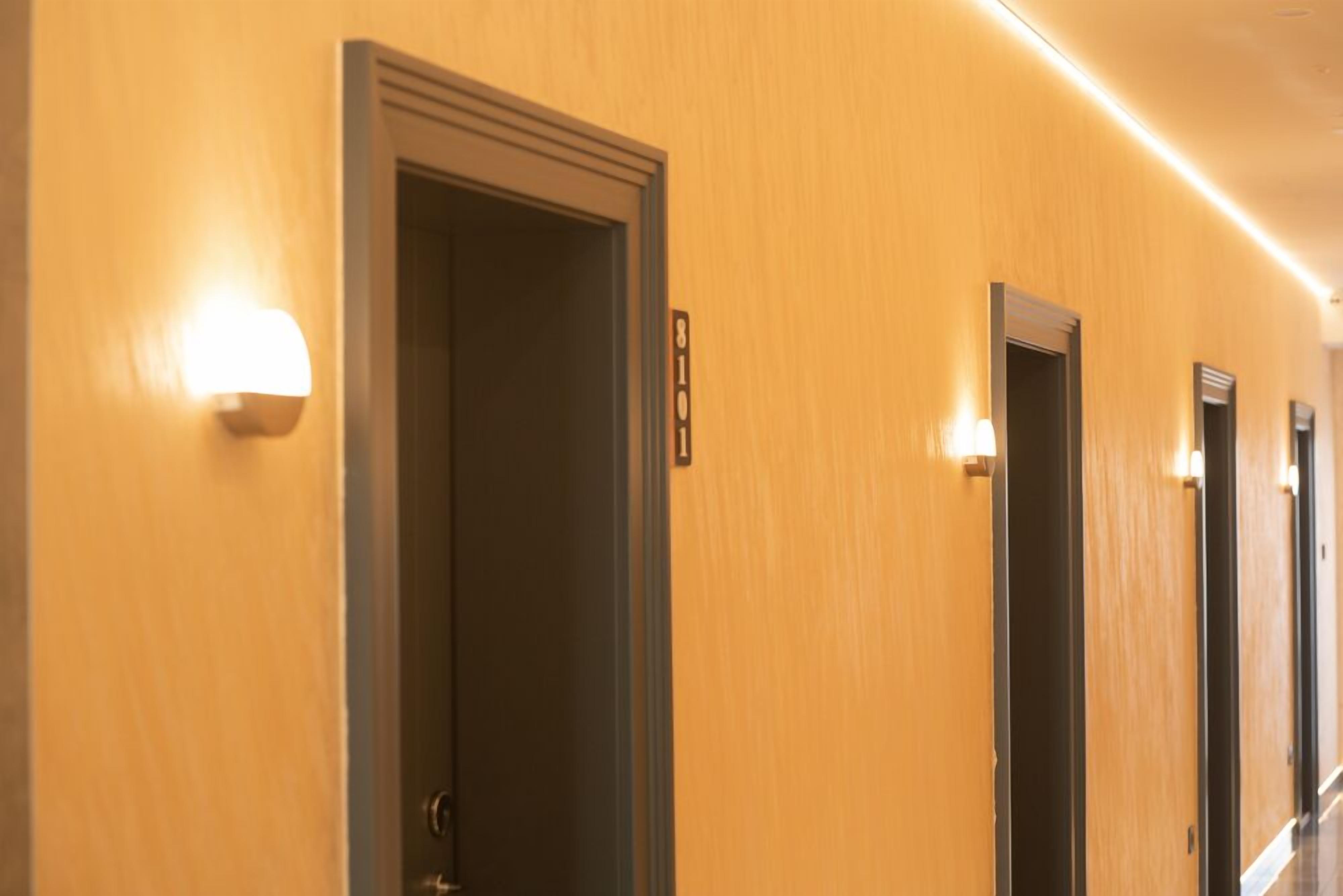 A hotel hallway with doors and wall-mounted light fixtures.