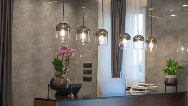 A modern reception desk with a vase of pink orchids, a potted plant, and a sleek, minimalist design. - KAME HOTEL BELGRADE (Belgrade)