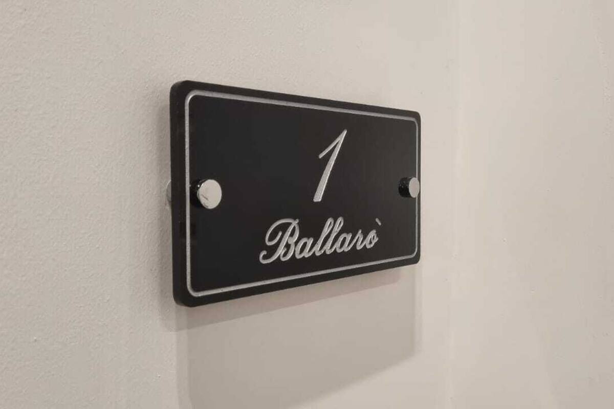 Een zwart bord met het cijfer 1 en de tekst 'Ballaro' op een witte muur.