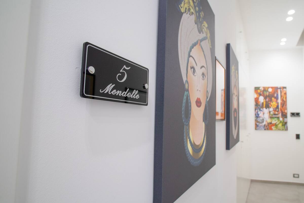 Een gang met een zwart bord waarop '5 Mondello' staat en een groot schilderij aan de muur.