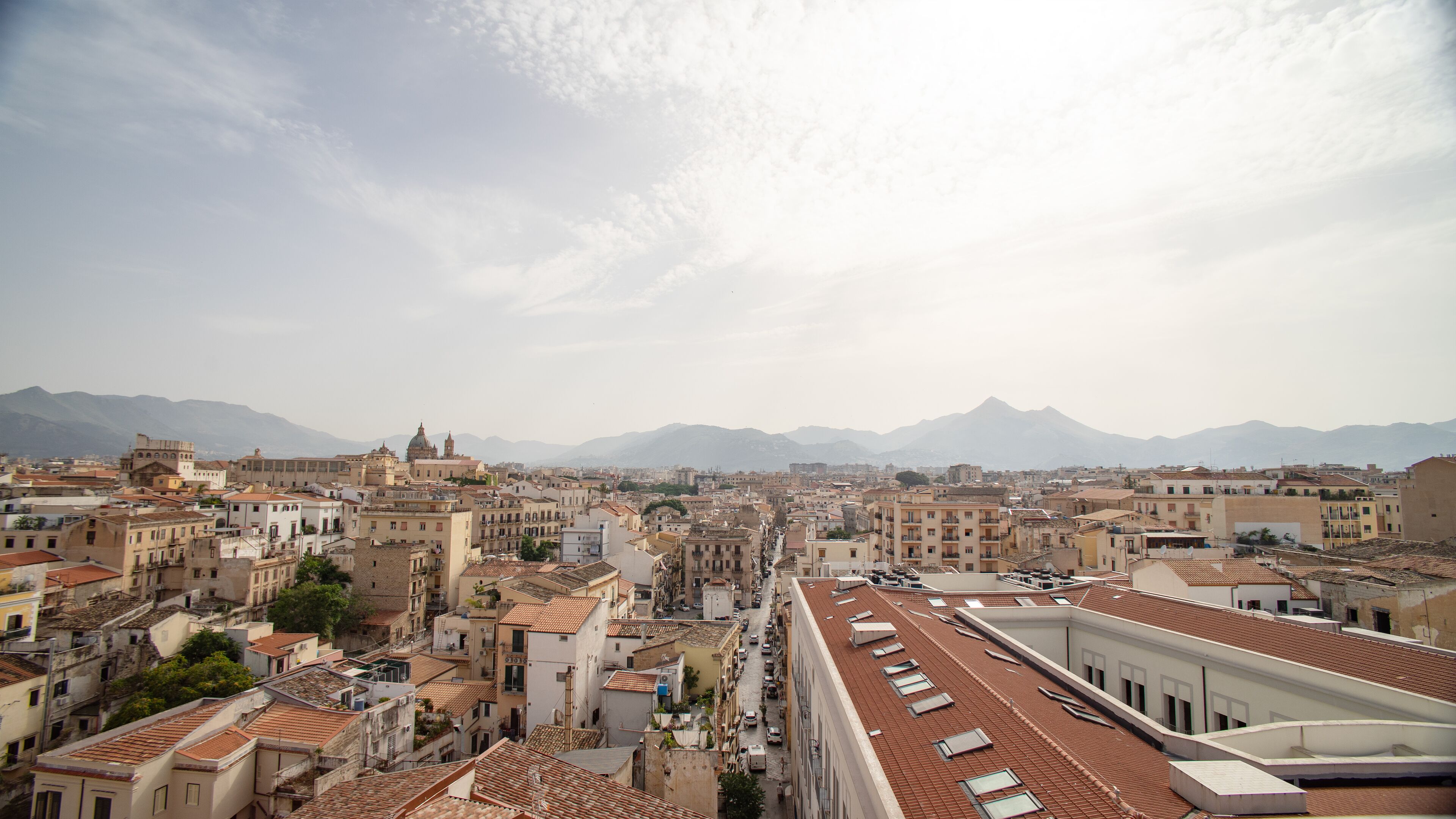 Un paysage urbain mêlant bâtiments historiques et modernes, avec un dôme imposant et une chaîne de montagnes en arrière-plan.
