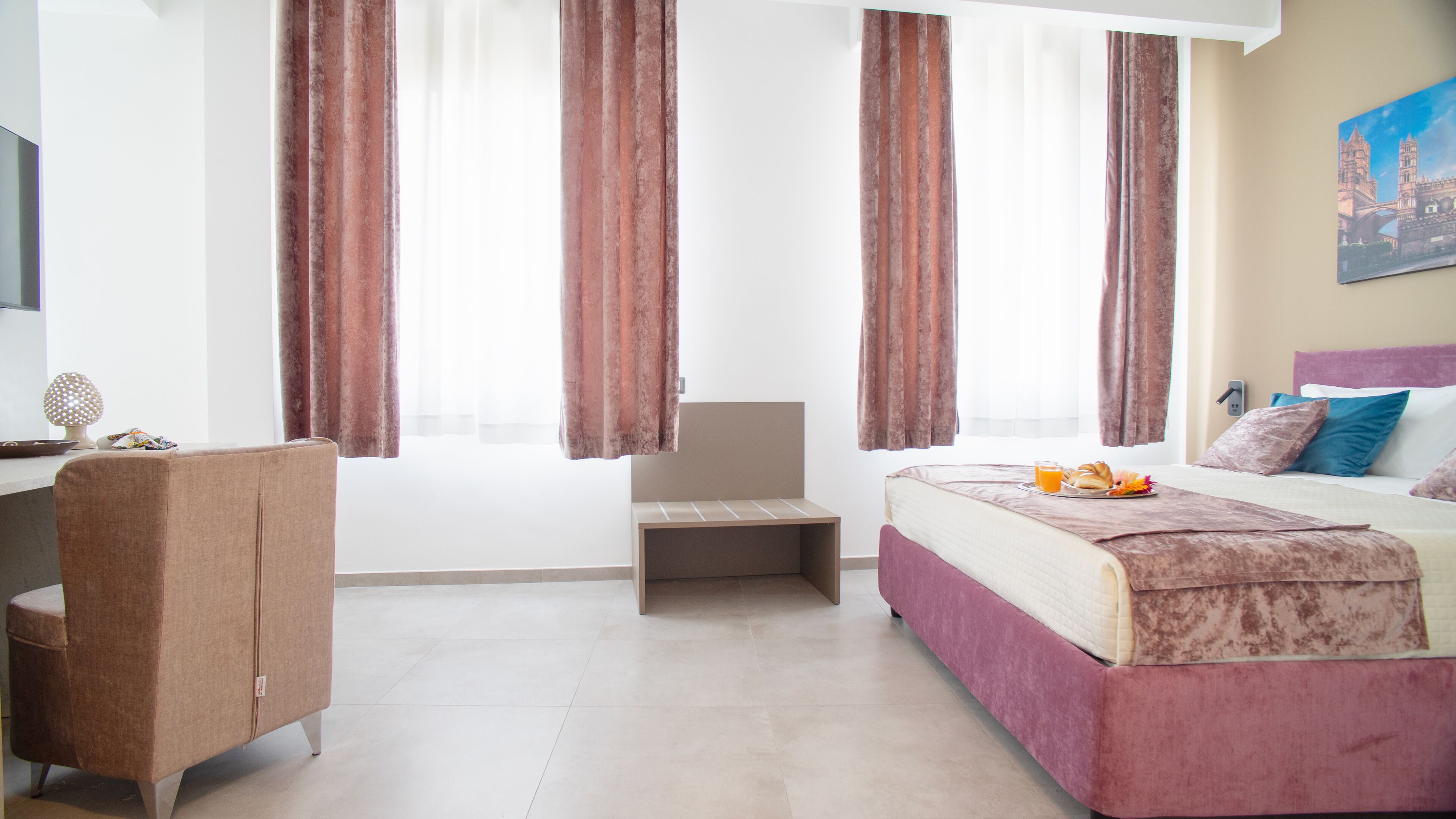 Een hotelkamer met een bed, bureau, stoel en raam met gordijnen.