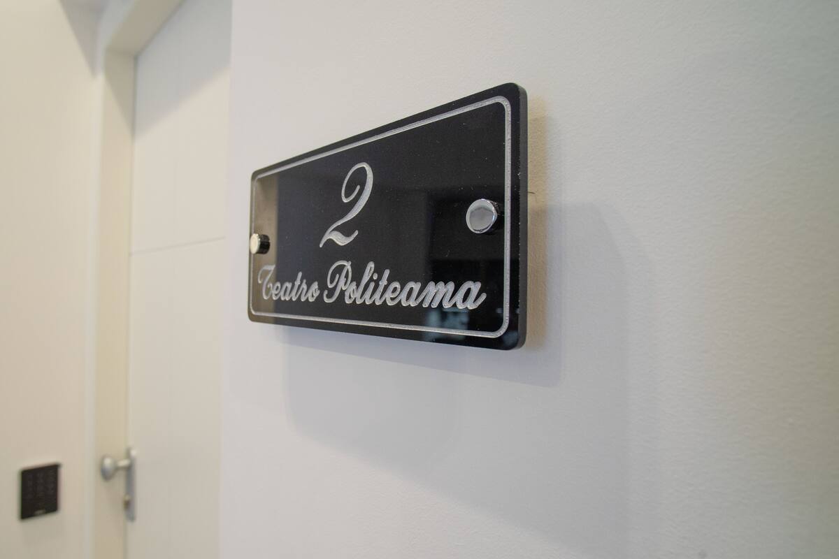 Een zwart metalen bord met het cijfer 2 en de tekst 'Teatro Politeama' op een witte muur.