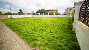 A grassy yard with a paved walkway, a white wall, and a building in the background. - 3 bedrooms | Entire Flat | Amasaman, Accra (Amasaman,)
