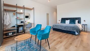 Una habitación de hotel moderna con una cama, dos sillas azules, un escritorio con un ordenador, un espejo y un armario.