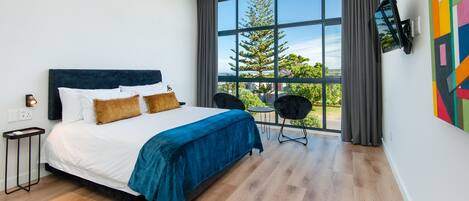 Een moderne slaapkamer met een groot bed, een aan de muur bevestigde televisie en uitzicht op bomen door het raam.