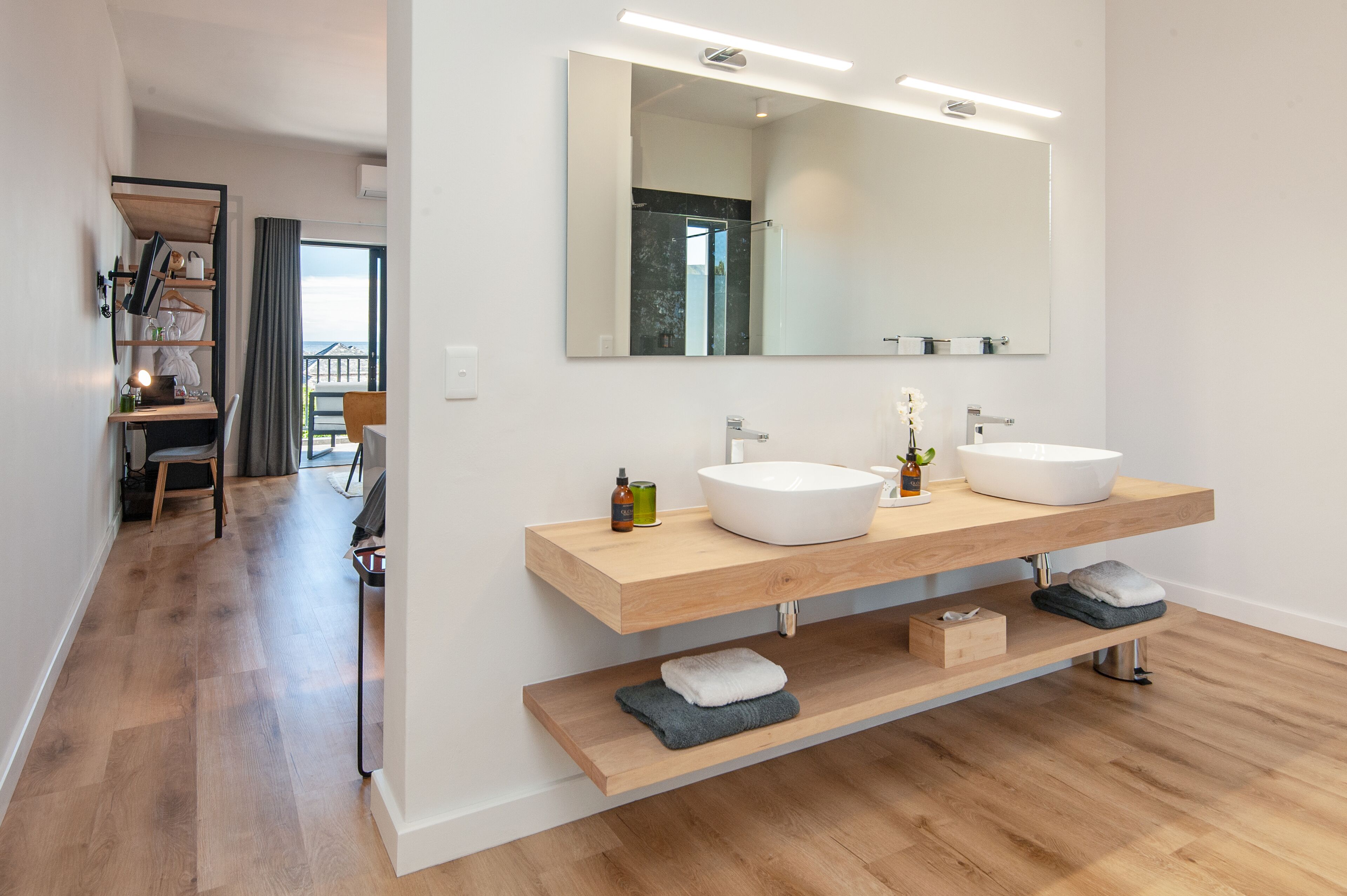 A modern bathroom with two sinks, a large mirror, and wooden shelves.