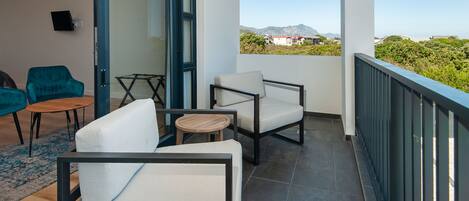 A balcony with two white cushioned chairs, a small round table, and a teal chair.