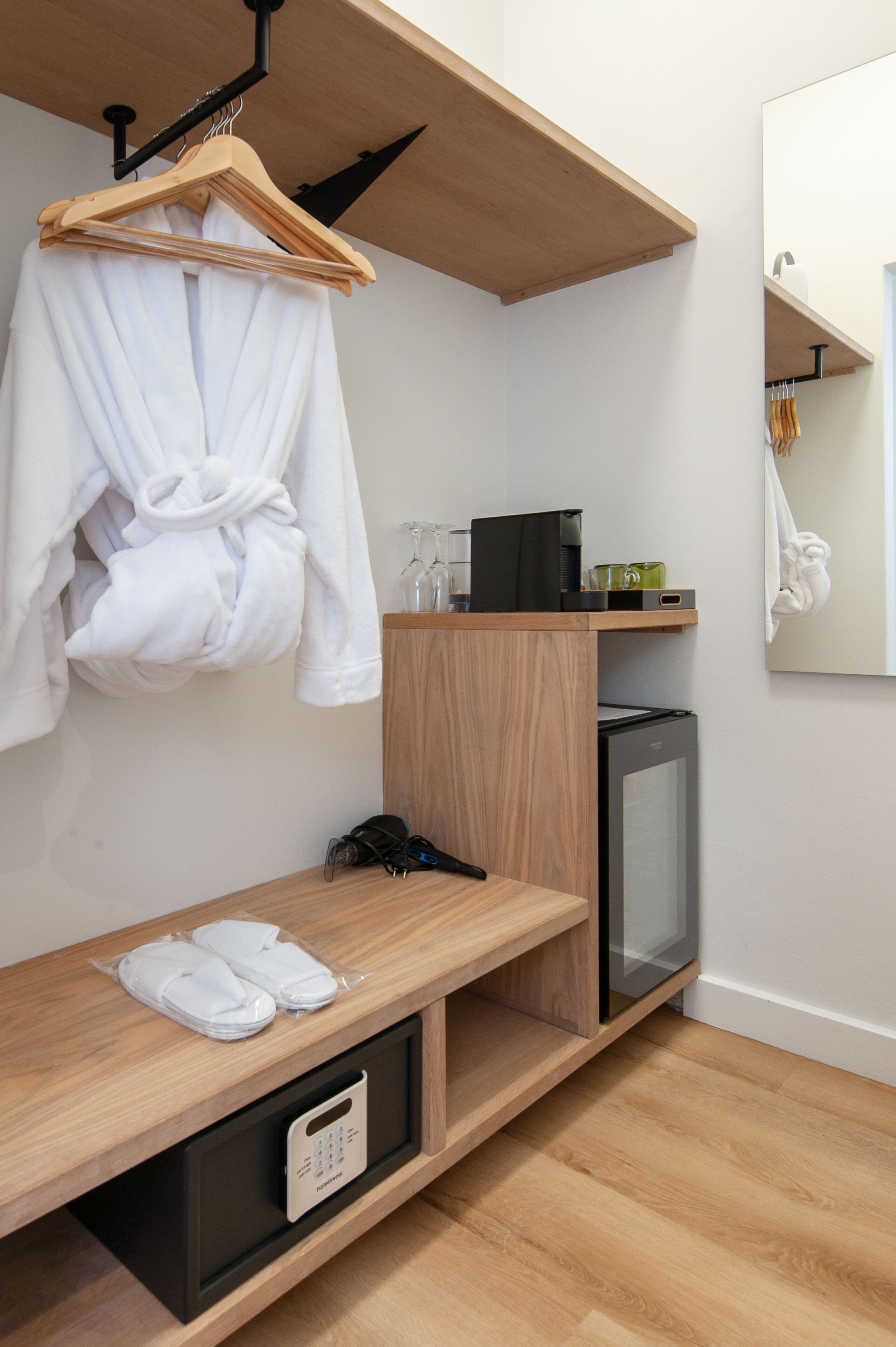 Una habitación de hotel moderna con un banco de madera, un refrigerador pequeño, un microondas y una bata colgada.