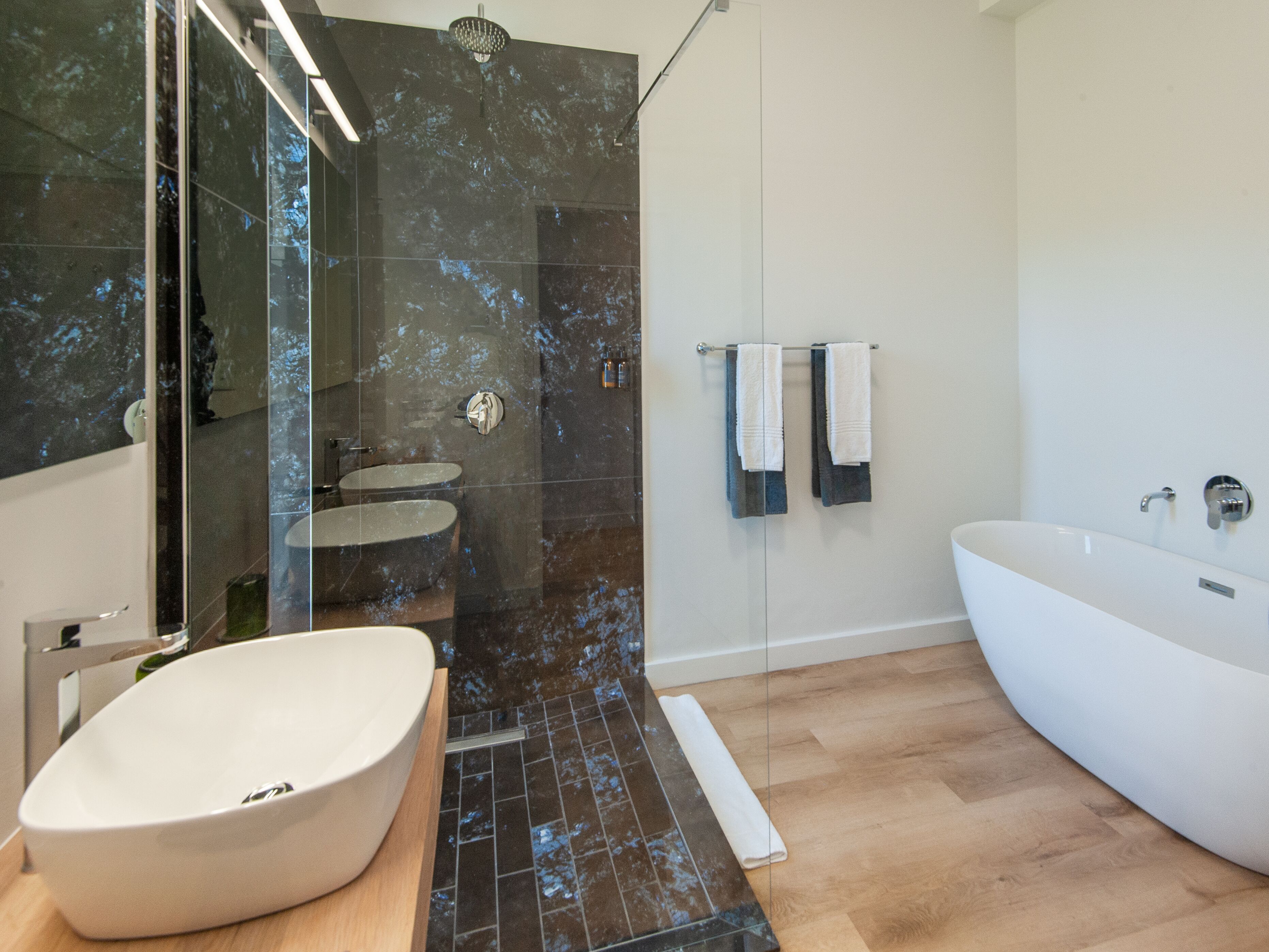 A modern bathroom with a freestanding bathtub, a large oval sink, and a glass-enclosed shower area.