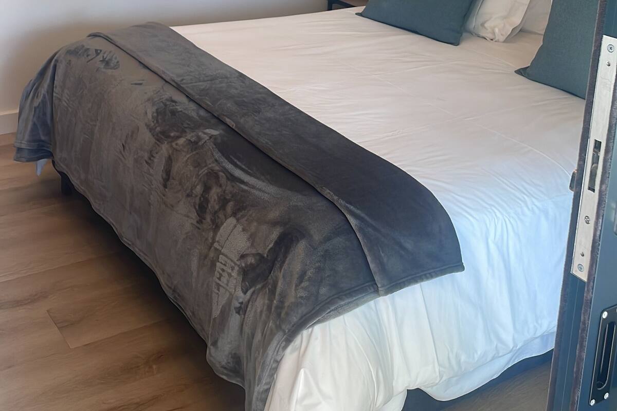 A bedroom with a bed, pillows, a nightstand, a painting, and a wooden floor.