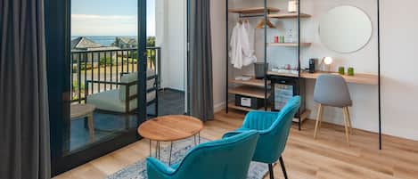 A modern room with a balcony, a desk with a chair, a round mirror, and a shelving unit with clothes and toiletries.