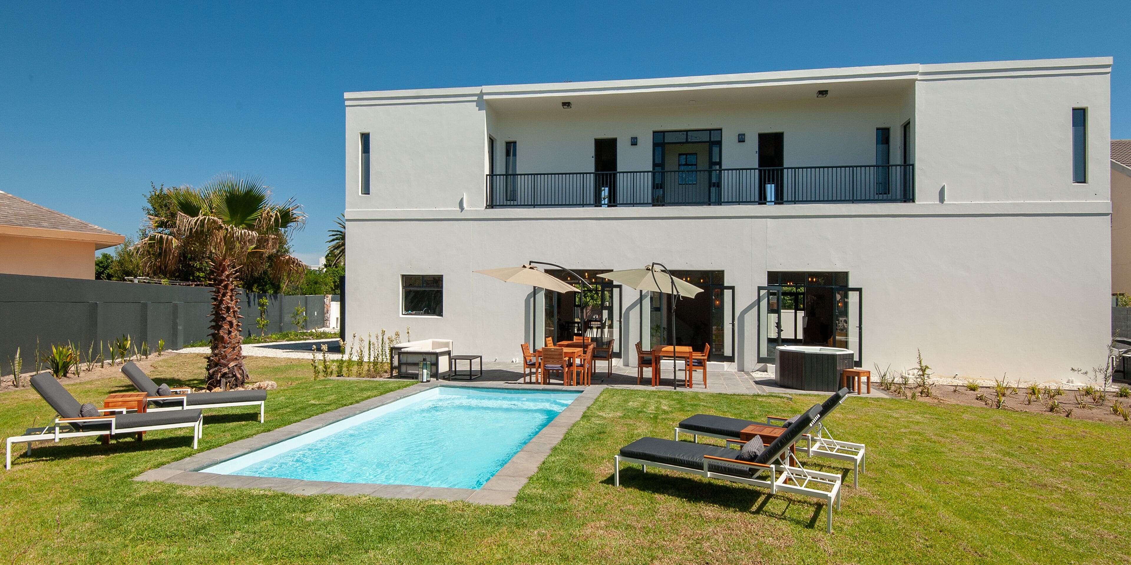 A modern two-story house with a swimming pool, outdoor seating, and a balcony.