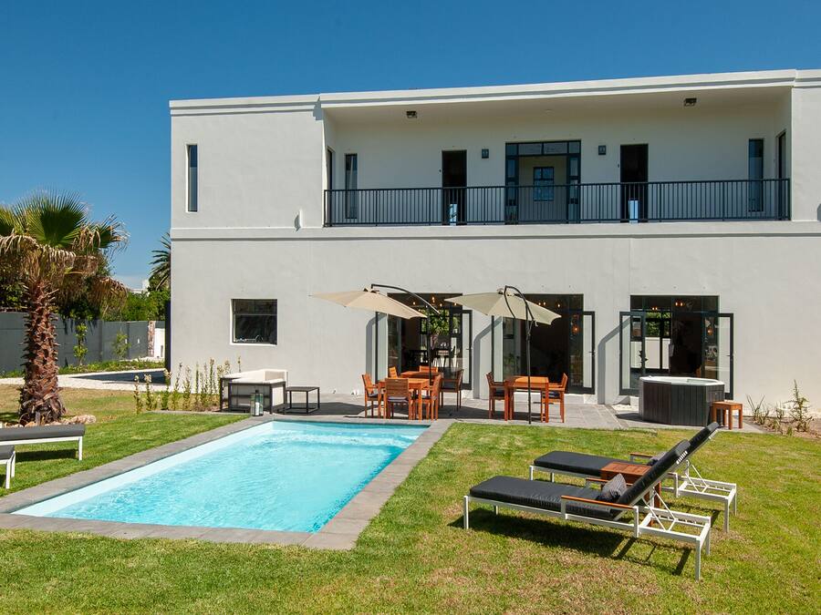 A modern two-story house with a swimming pool, outdoor seating, and a balcony.