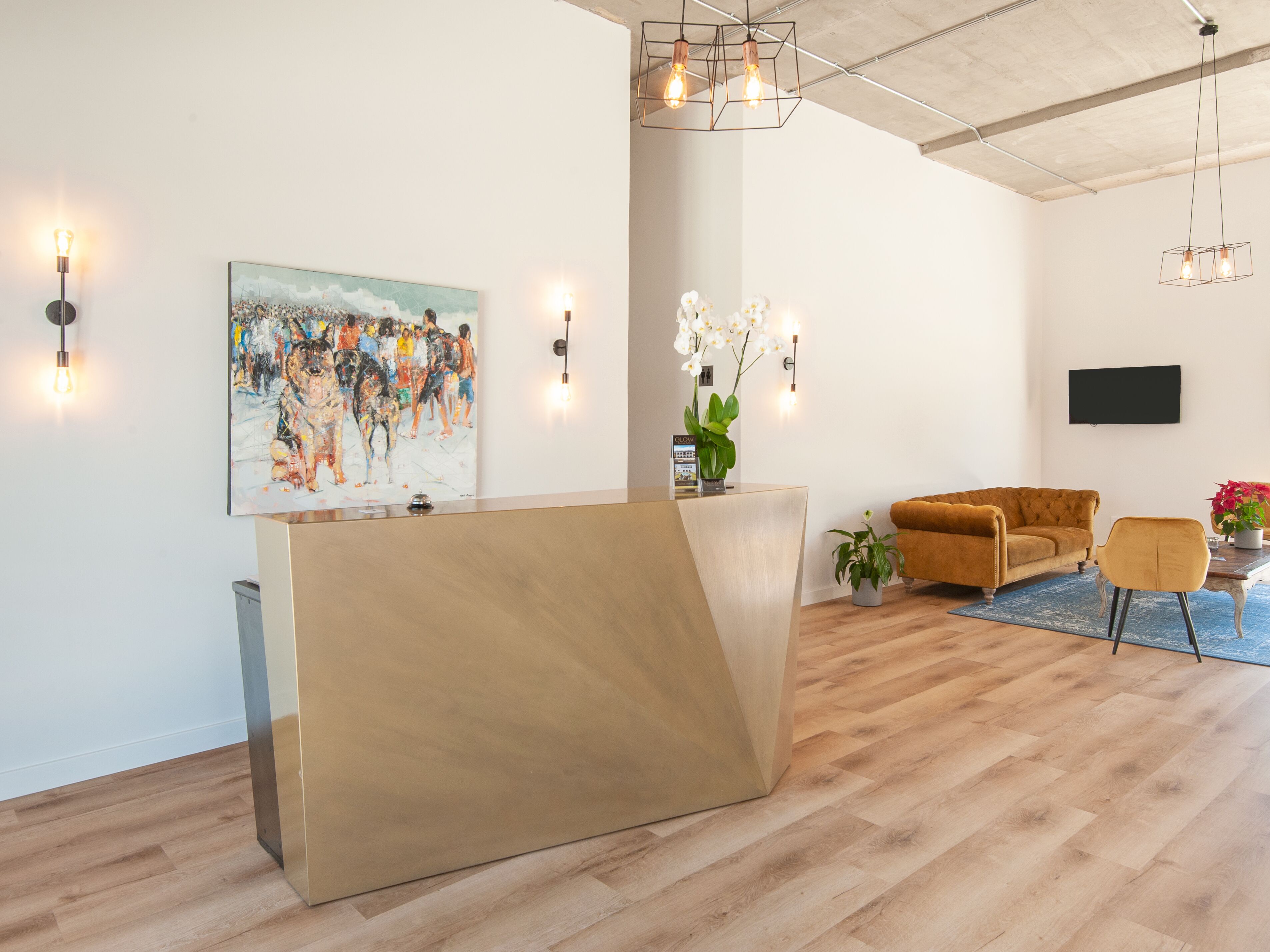 A modern reception area with a wooden reception desk, a large abstract painting, a sofa, and a TV mounted on the wall.