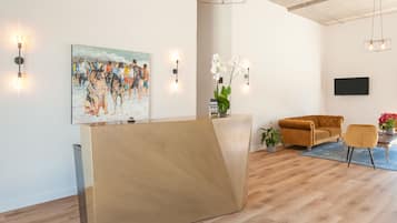 A modern reception area with a wooden reception desk, a large abstract painting, a sofa, and a TV mounted on the wall.