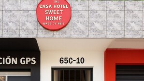 Ein Hotel Eingang mit einem Schild, auf dem 'THE CASA HOTEL SWEET HOME' steht, und einer Tür mit der Bezeichnung '65C-10'.