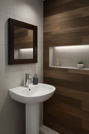 Une salle de bain moderne avec un lavabo sur colonne blanc, un miroir et une étagère ornée d’une petite plante.