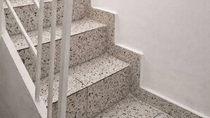 Eine Treppe mit weißen Geländern und gefleckten Stufen, ein gerahmtes Pflanzenbild an der Wand und ein Blumentopf im Treppenabsatz.