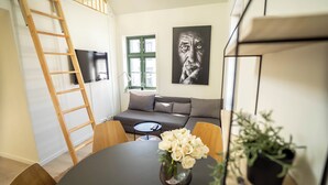 A living room with a round table, a sofa, a TV, a window, and a painting. - Vibrant Apartment on Bustling Street, Above a Restaurant - Perfect for Tourists, (Stavanger)