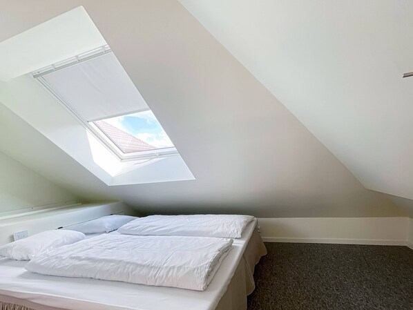 A room with a skylight, a bed with white bedding, and a carpeted floor. - Vibrant Apartment on Bustling Street, Above a Restaurant - Perfect for Tourists, (Stavanger)