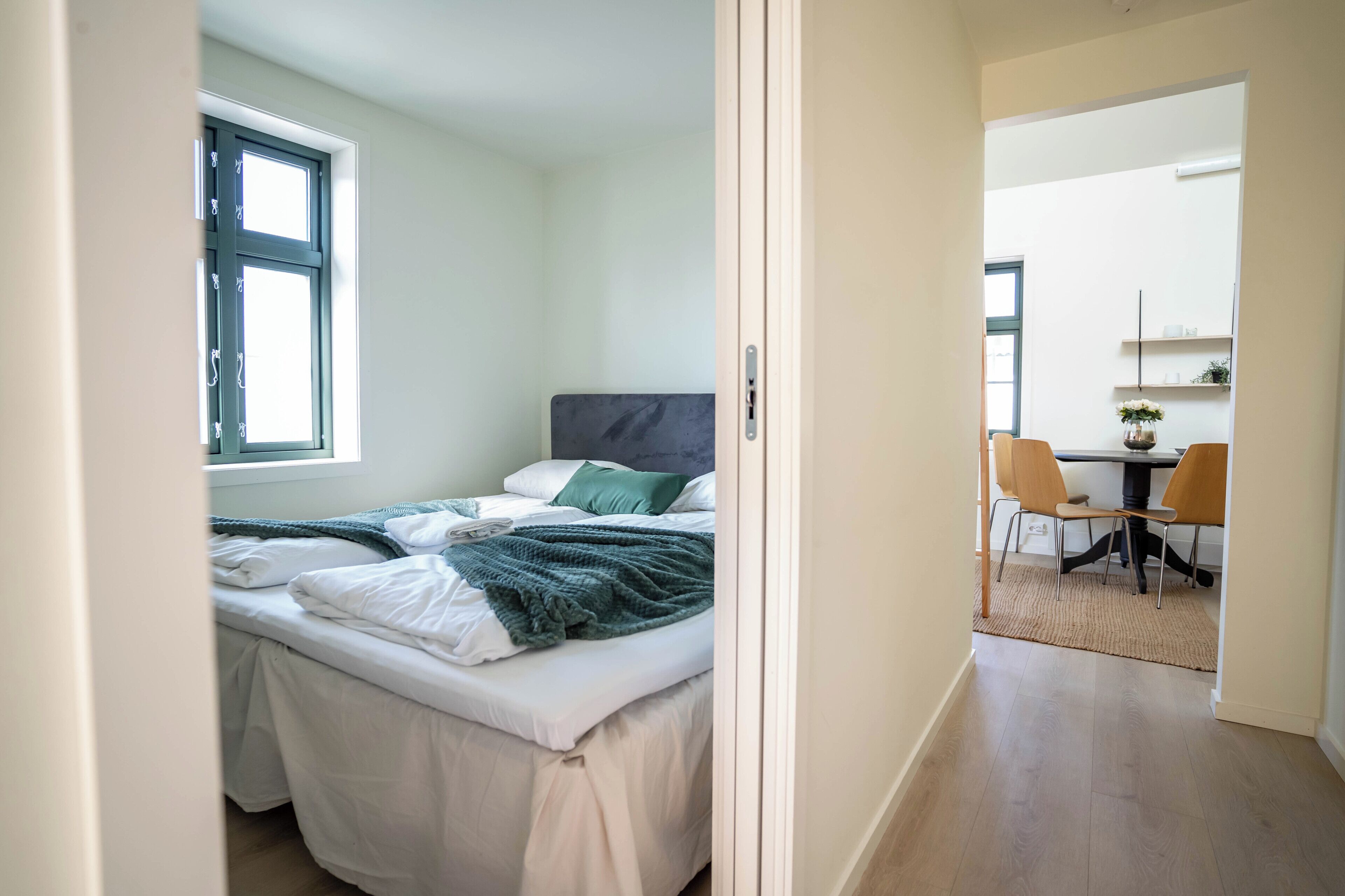 Un dormitorio con cama, ventana, escritorio con sillas y una mesita con un florero.
