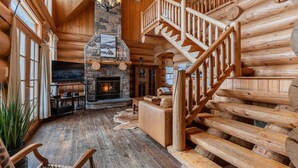 A log cabin interior with a stone fireplace, wooden staircase, and a cozy seating area. - Fiddler Lake Resort - Bear 10 (Mille-Isles)