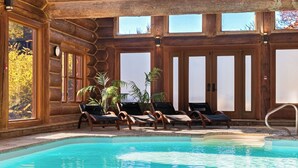 Una cabaña de madera con piscina, sillones de descanso y grandes ventanales.