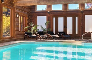 A log cabin with a pool, lounge chairs, and large windows.