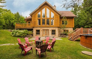 A log cabin with a deck, a hot tub, and a fire pit in the backyard.