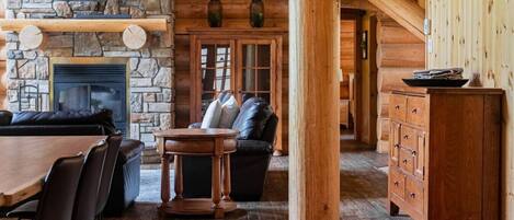L’intérieur d’une cabane en rondins, avec une cheminée en pierre, des meubles en bois et un téléviseur fixé au mur.