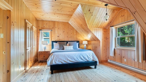 A bedroom with a bed, bedside lamps, a window, and wooden walls.