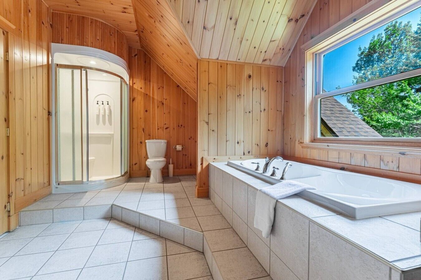 Interior de madera con inodoro, bañera y ventana con vista a árboles.