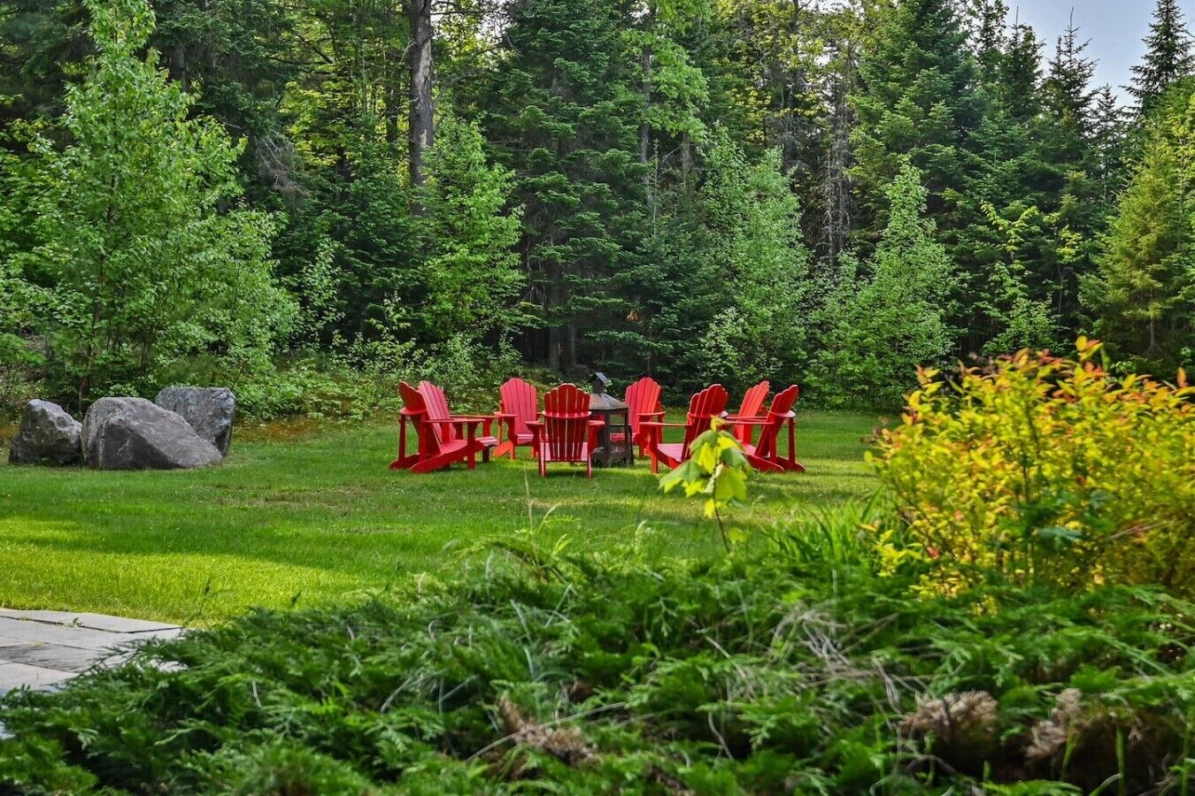 Un jardin avec des chaises rouges et une table, entouré d’arbres et de rochers.