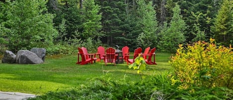 Un jardín con sillas rojas y una mesa, rodeado de árboles y rocas.
