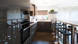 Cozinha moderna com eletrodomésticos de aço inoxidável, um espaço bar com banquetas e uma janela grande que traz luz natural.