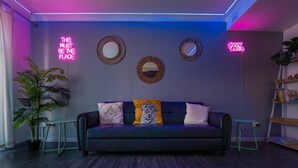 Uma sala de estar moderna com um sofá escuro, duas molduras espelhadas e letreiros luminosos nas paredes.
