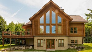 A log cabin with a large front porch, a deck, and a stone foundation.