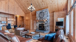 Een chaletinterieur met een stenen open haard, lederen meubels en een televisie.