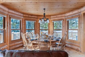 A wooden cabin with a dining area featuring a round table, chairs, and a chandelier.