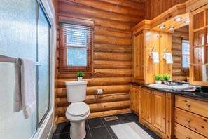 A log cabin bathroom with a toilet, sink, and wooden cabinets.