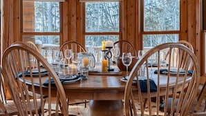 Een houten eettafel voor zes personen, compleet met stoelen, grote ramen en uitzicht op bomen.