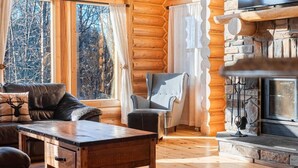 A log cabin interior with a fireplace, leather sofa, and a stone fireplace surround. - Fiddler Lake Resort - Deer 9 (Mille-Isles)