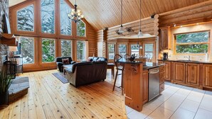 A log cabin interior with a dining area, kitchen, and large windows. - Fiddler Lake Resort - Deer 30 (Mille-Isles)